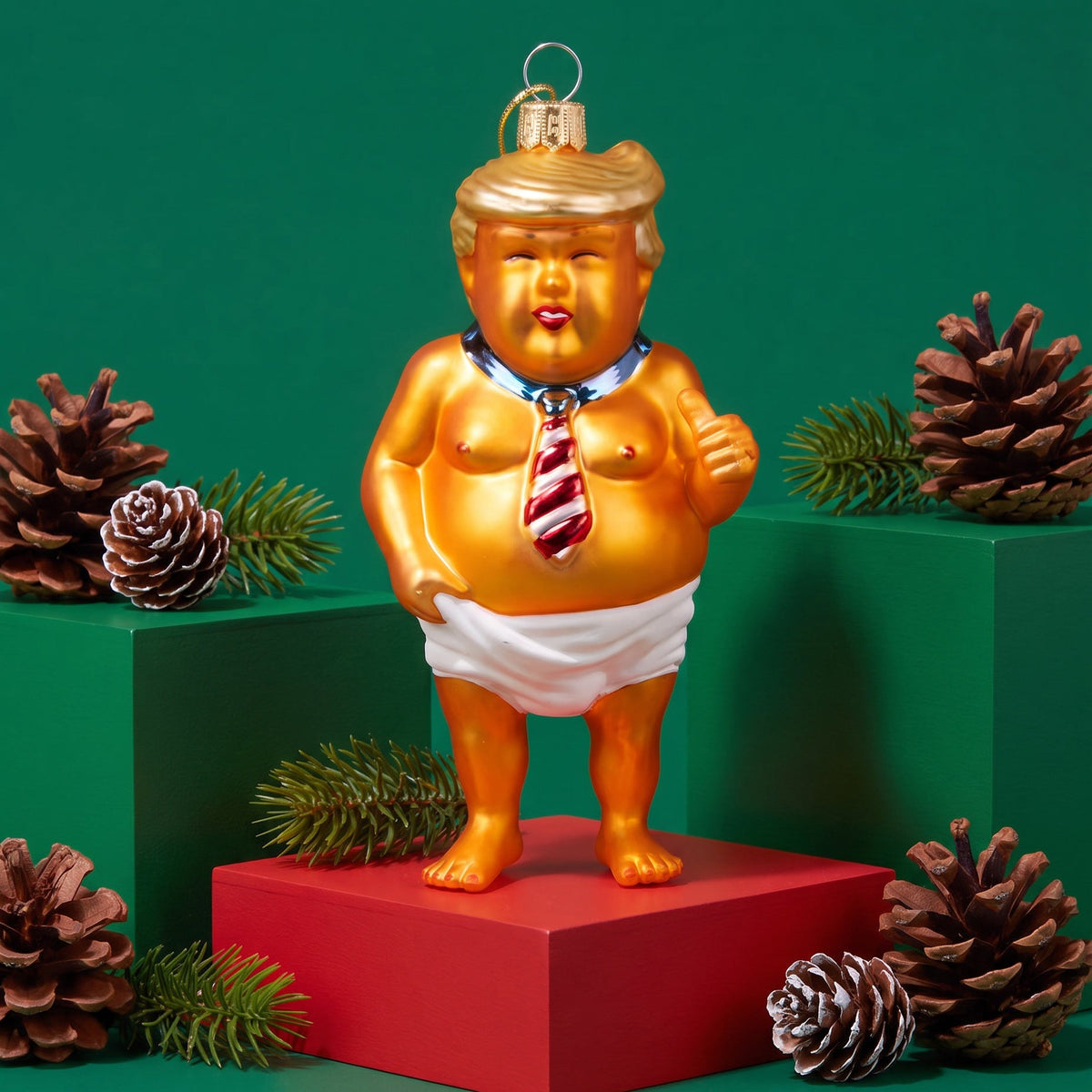 A novelty Christmas ornament shaped like a caricature of Donald Trump, standing on a red pedestal against a green background with pinecones and greenery.